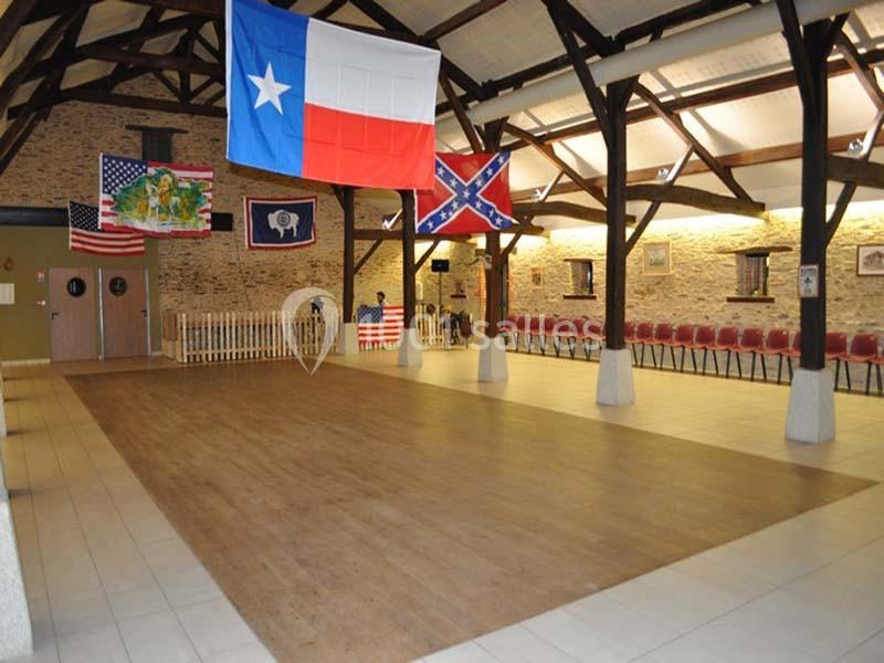 Salle avec parquet, drapeaux américains et confédérés suspendus, rangées de chaises contre des murs en pierre.