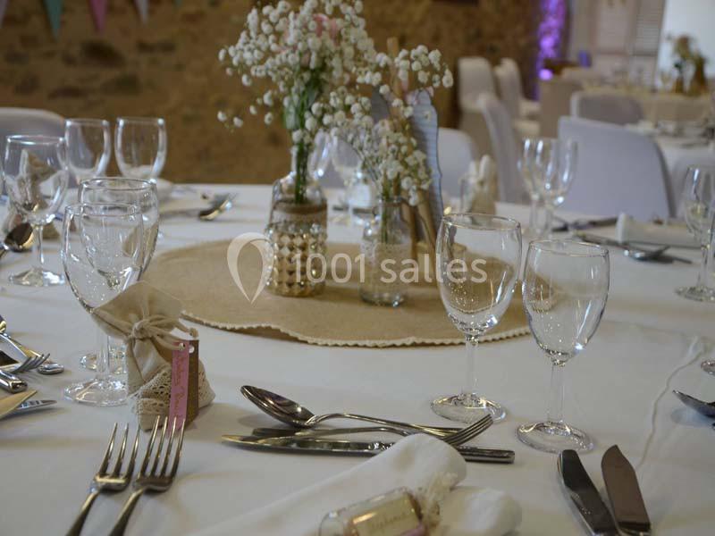Table décorée pour un mariage avec nappes blanches, verres, couverts, et centre de table floral sur napperon en toile de…