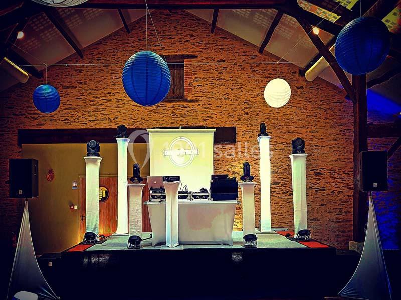 Scène de DJ dans une salle en pierre avec éclairage coloré, lanternes suspendues et colonnes lumineuses blanches.