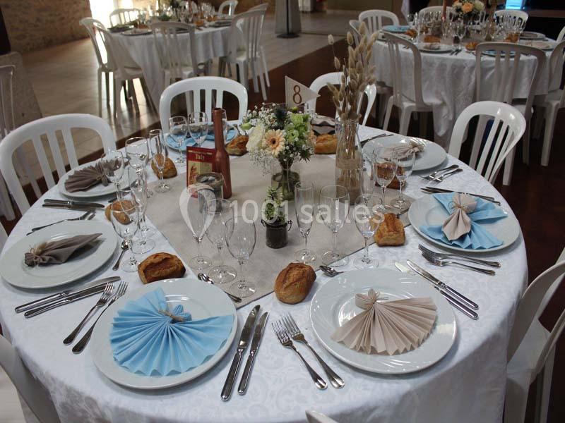 Table ronde dressée pour un repas, avec nappes blanches, serviettes pliées, couverts, verres et décorations florales.