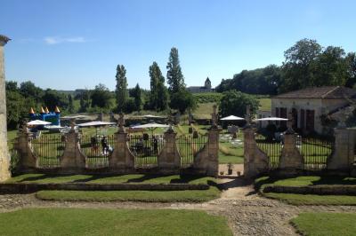 Château ancien avec deux tours rondes, vu depuis une grille en fer forgé ouverte, sous un ciel bleu.