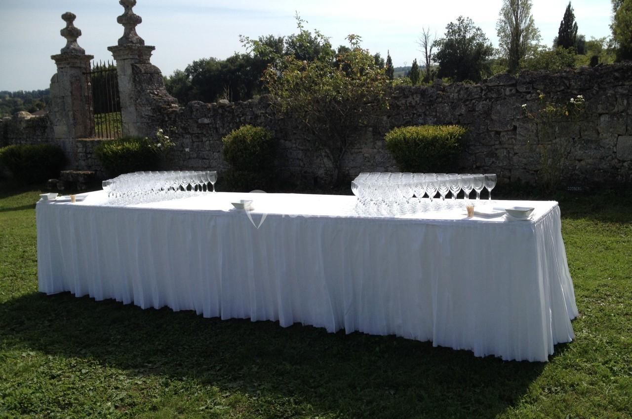 Table longue drapée de blanc, disposée en extérieur sur une pelouse, avec des rangées de verres à pied alignés.