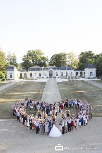 Un groupe de personnes formant un cœur devant un grand bâtiment blanc entouré de jardins.