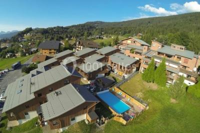 Piscine extérieure avec baigneurs, entourée de bâtiments en bois et de montagnes verdoyantes en arrière-plan.
