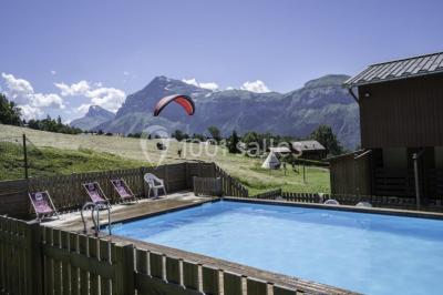 Piscine extérieure avec baigneurs, entourée de bâtiments en bois et de montagnes verdoyantes en arrière-plan.