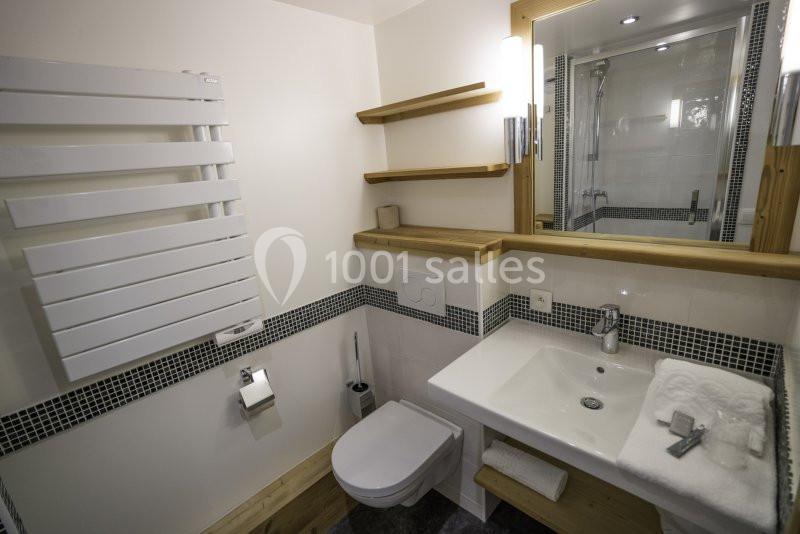 Salle de bain moderne avec lavabo, toilettes, miroir, étagères en bois, sèche-serviettes et douche en arrière-plan.