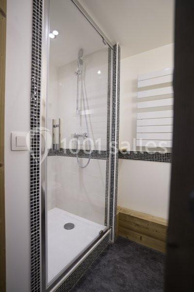 Douche moderne avec parois vitrées, carrelage noir et blanc, pommeau mural et sèche-serviettes blanc.