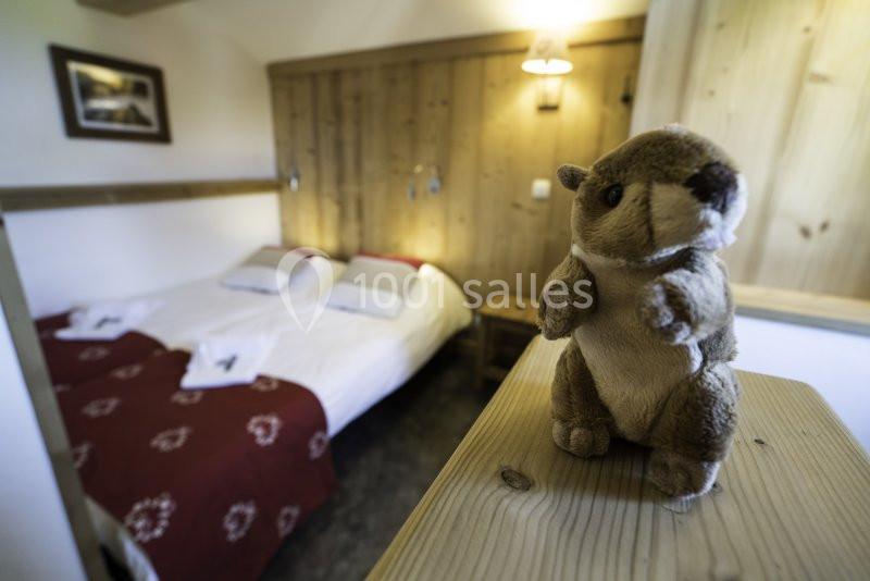 Une chambre cosy avec lit double, décoration en bois et une peluche de marmotte posée au premier plan.