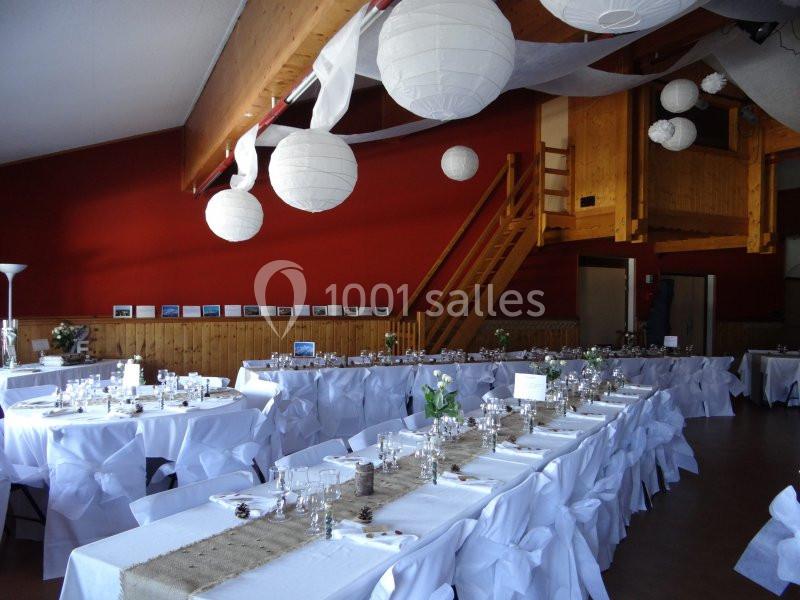Salle décorée pour un événement, avec tables dressées, nappes blanches, chemins de table en toile de jute et lanternes…