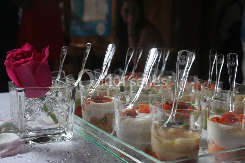 Verrines variées disposées sur un plateau en verre, accompagnées d'une rose rose dans un vase transparent.