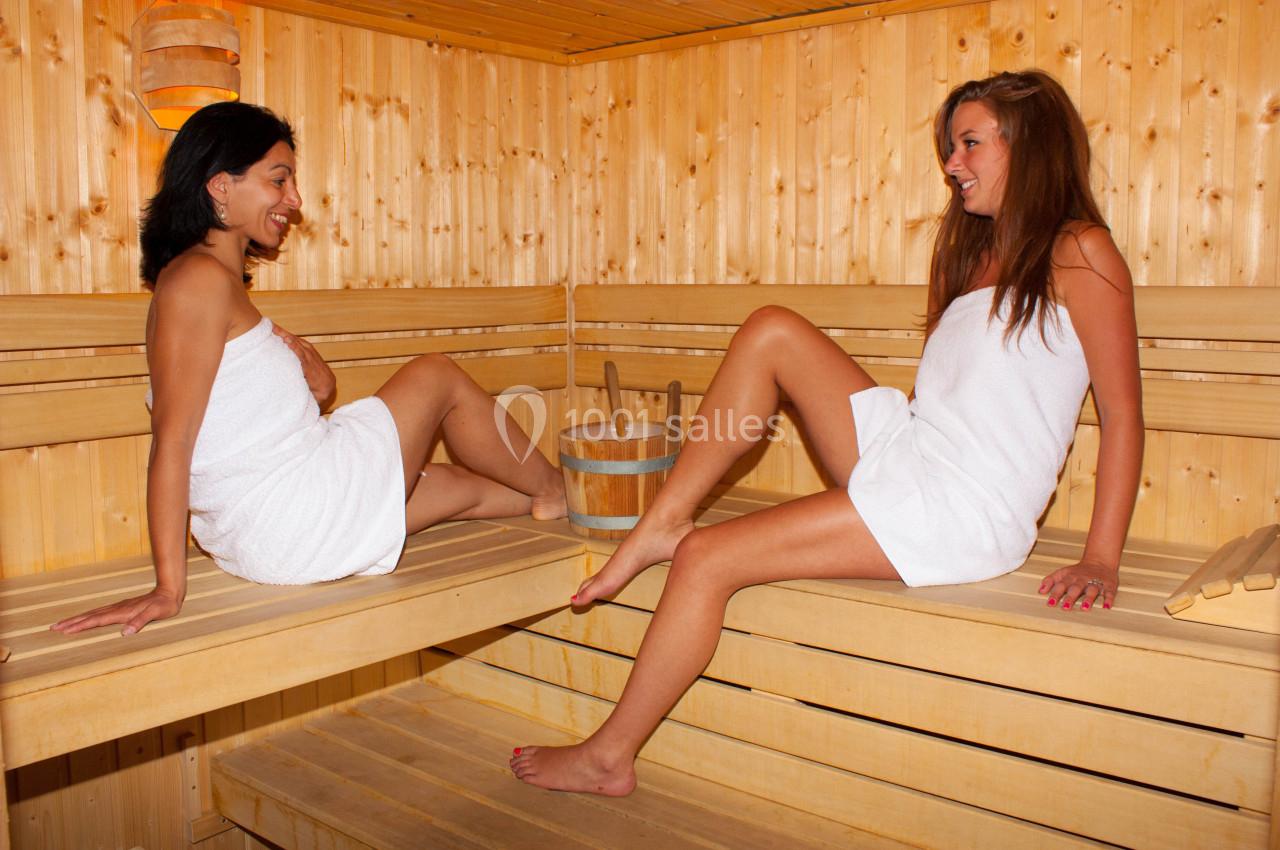 Deux femmes en serviettes discutent et se détendent dans un sauna en bois lumineux.