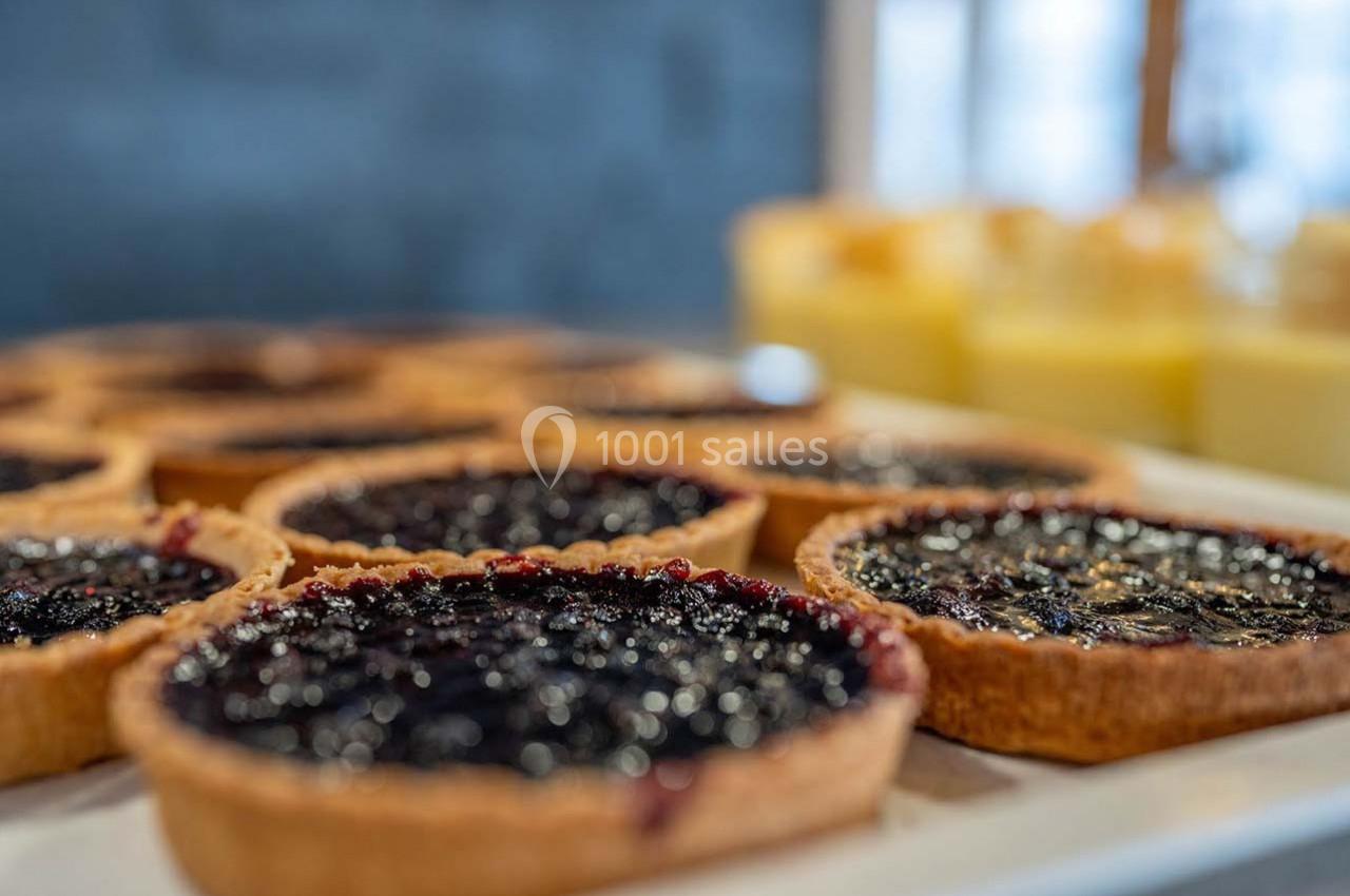 Tartes aux myrtilles alignées sur un plateau, avec des desserts jaunes flous en arrière-plan.