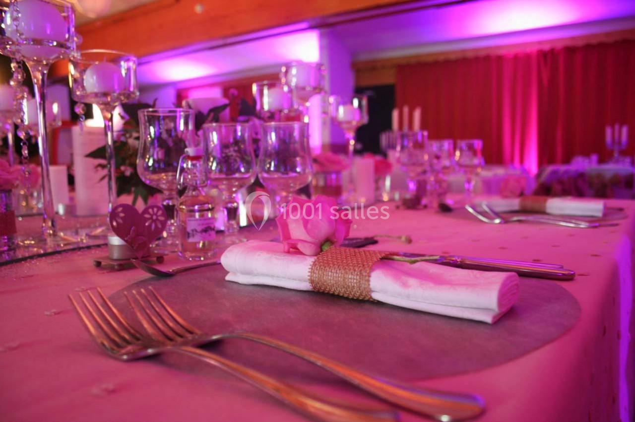 Table élégamment dressée avec des couverts, des verres et une décoration rose sous un éclairage tamisé.