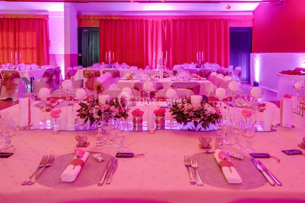 Salle de réception décorée en rose avec tables dressées, compositions florales et bougies pour un événement festif.