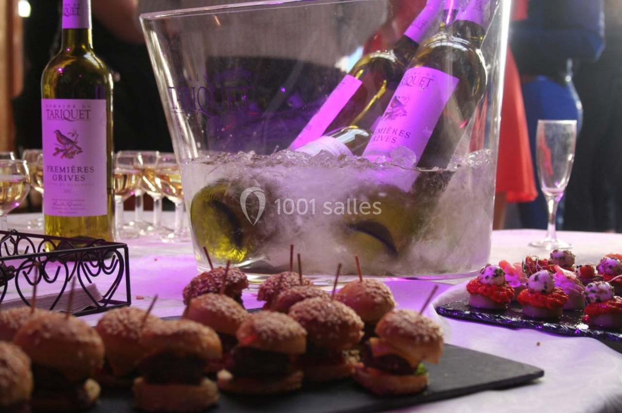 Bouteilles de vin blanc dans un seau à glace, entourées de verres et d'amuse-bouches sur une table.