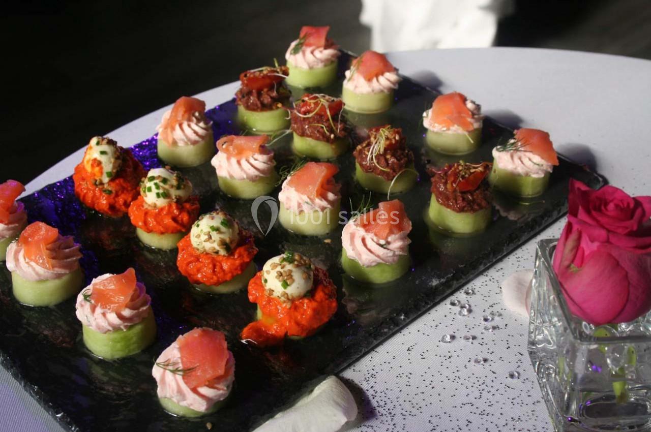 Plateau de bouchées apéritives variées sur une table, avec des garnitures colorées et une rose en décoration.