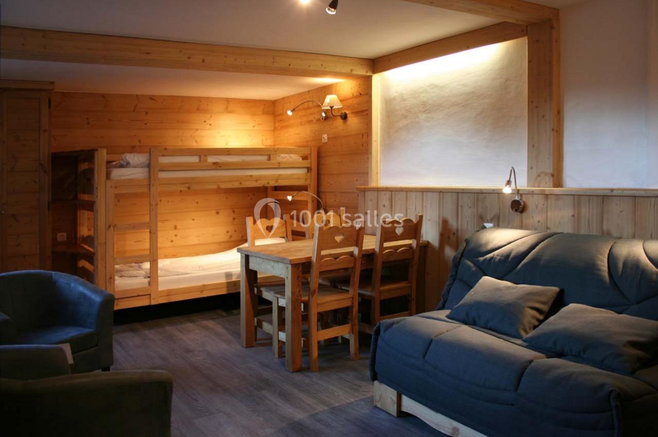 Salon en bois avec canapé, table à manger, chaises, lits superposés et éclairage chaleureux.