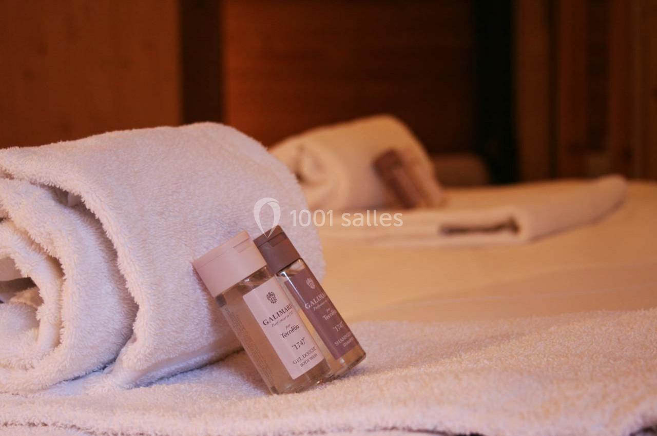 Deux serviettes blanches pliées avec des flacons de produits de toilette posés sur un lit dans une chambre chaleureuse.