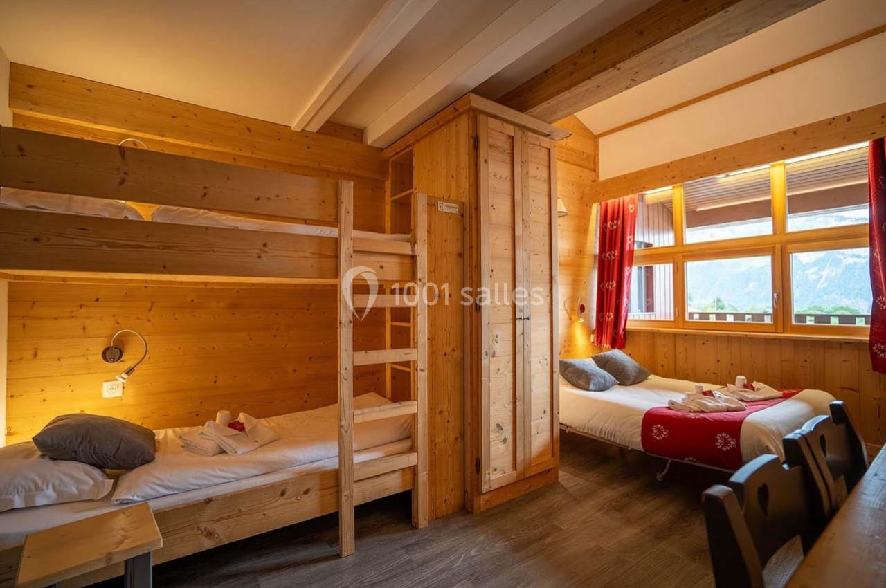 Chambre en bois avec lits superposés, lit double, fenêtre donnant sur une vue montagneuse et lumière naturelle.