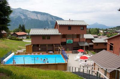 Piscine extérieure avec baigneurs, entourée de bâtiments en bois et de montagnes verdoyantes en arrière-plan.