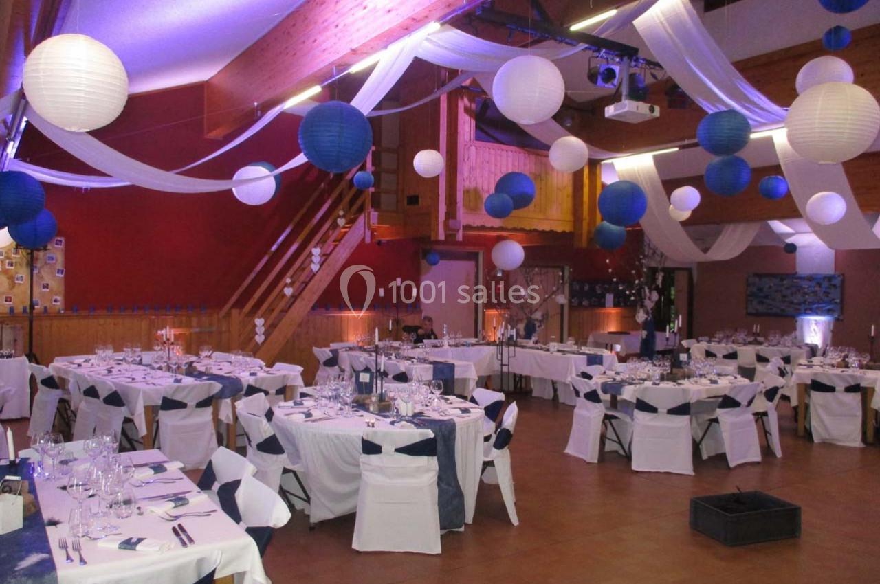 Salle de réception décorée avec des tables dressées, des lanternes suspendues et des drapés blancs et bleus.