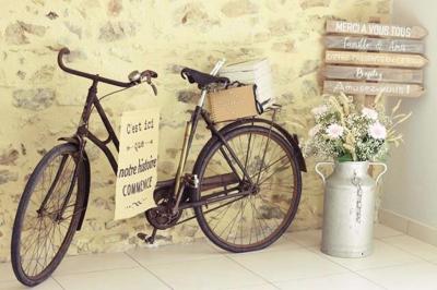 Voiture ancienne blanche décorée de fleurs, stationnée devant un bâtiment en pierre avec un toit en ardoise.