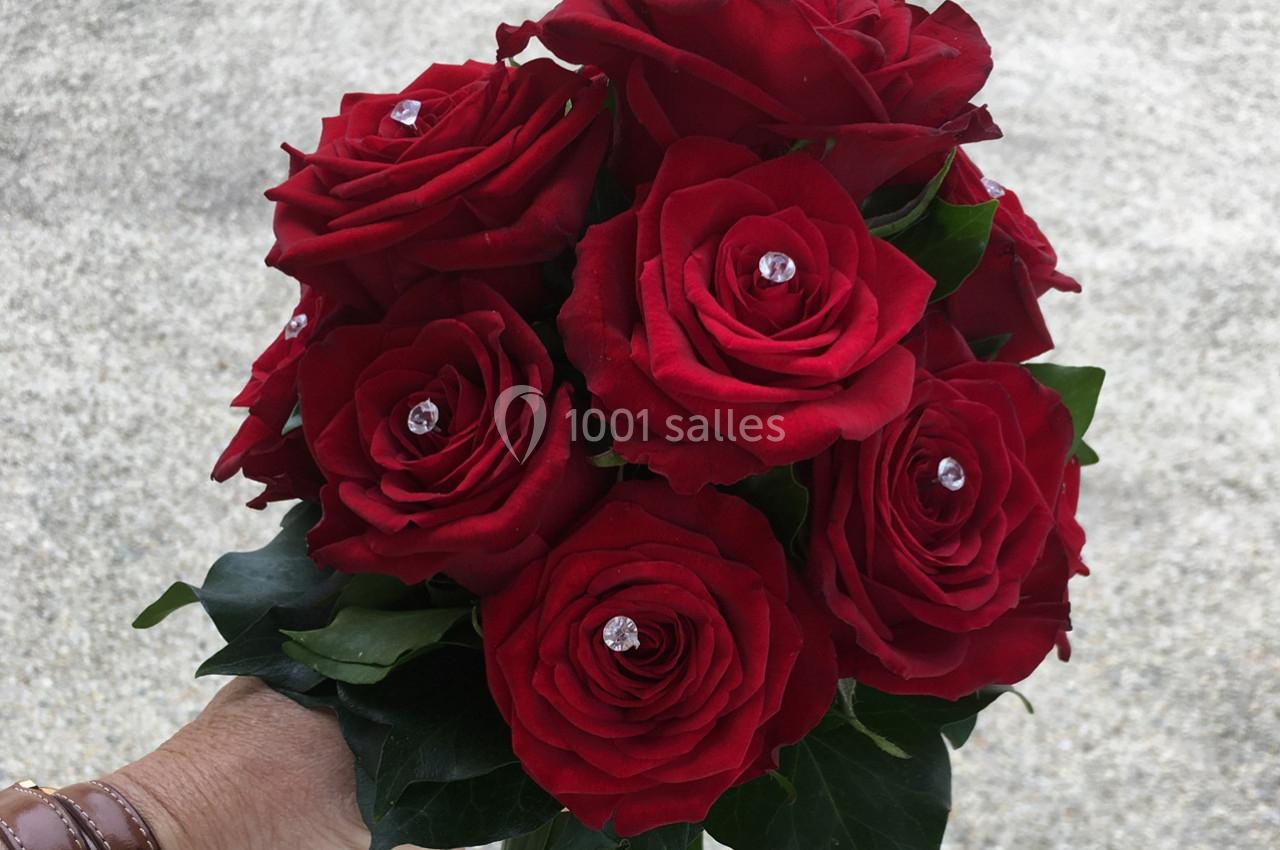 Bouquet de roses rouges ornées de perles brillantes, tenu par une main sur un fond gris clair.