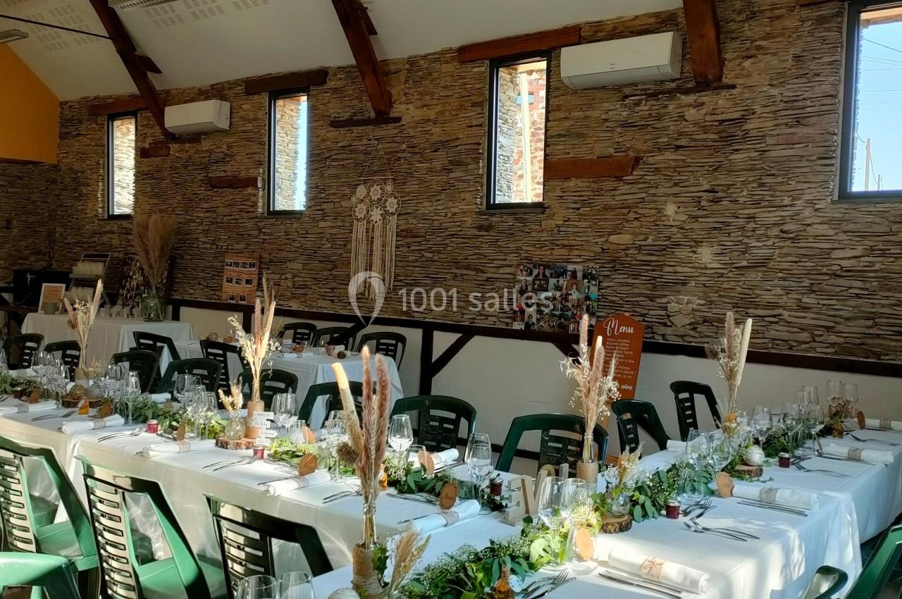 Salle de réception décorée avec des tables alignées, nappes blanches, centres de table végétaux et chaises vertes.