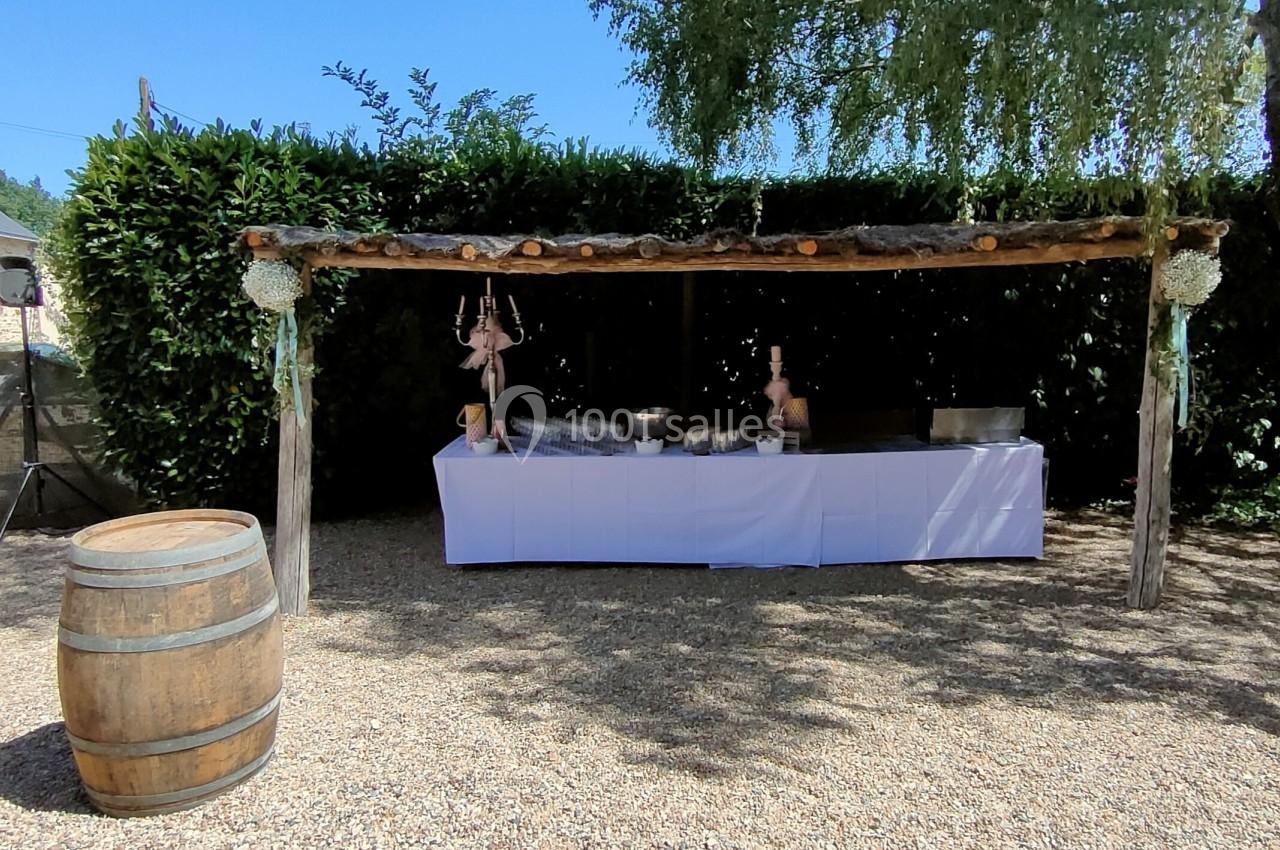 Table de buffet décorée sous une pergola en bois, entourée de verdure, avec un tonneau en premier plan.
