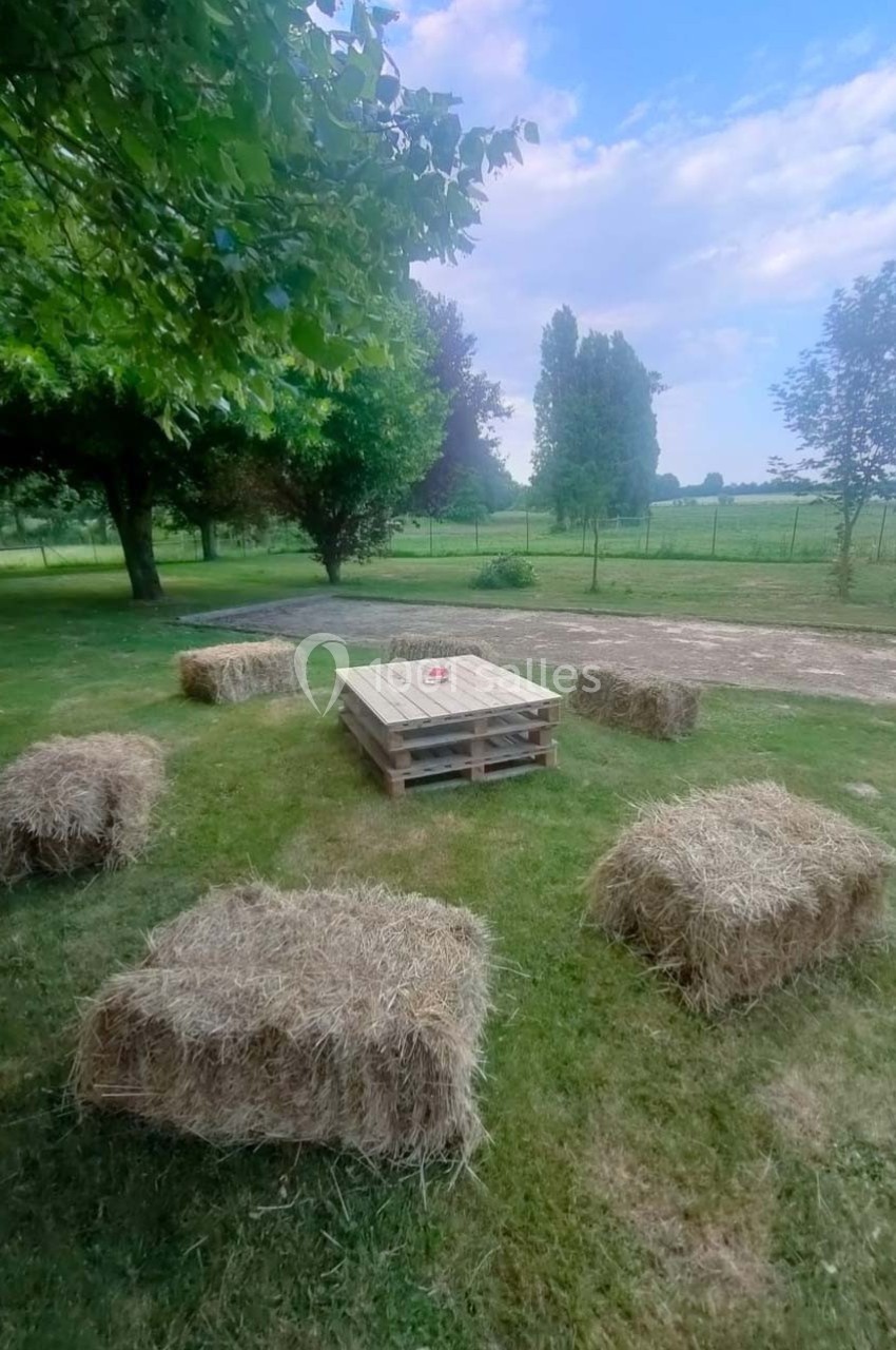 Bottes de paille disposées autour d'une table basse en palettes sur une pelouse, avec des arbres et un chemin en arrière…