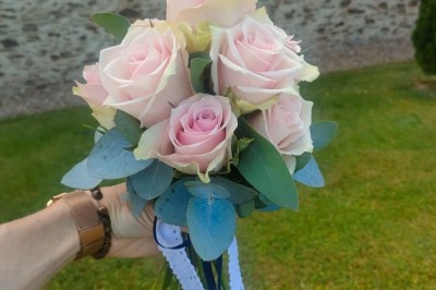 Voiture ancienne blanche décorée de fleurs, stationnée devant un bâtiment en pierre avec un toit en ardoise.