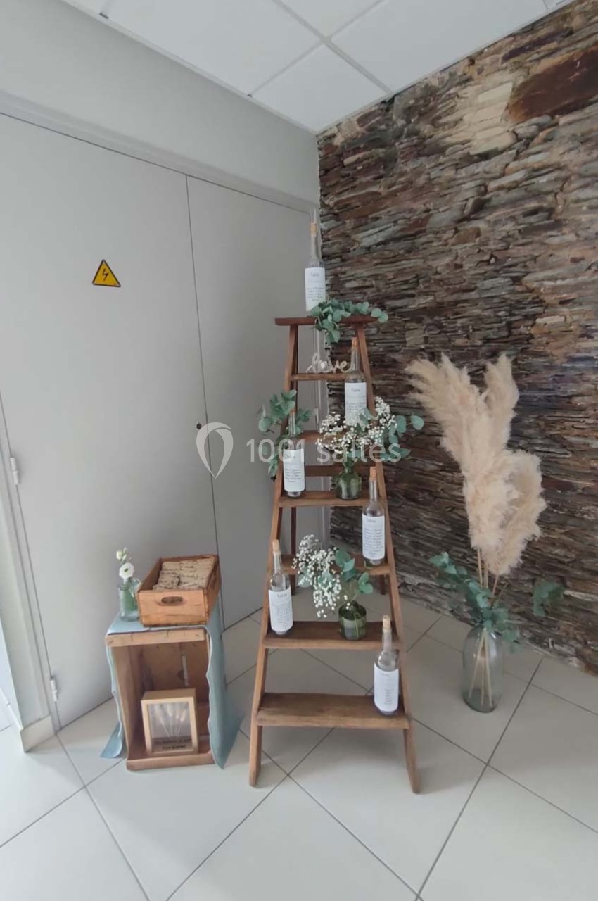 Échelle en bois décorée de fleurs blanches et feuillages, avec des pampas et caisses en bois sur un sol carrelé.