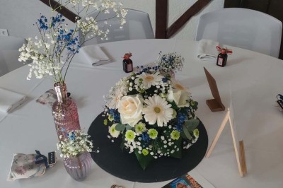Voiture ancienne blanche décorée de fleurs, stationnée devant un bâtiment en pierre avec un toit en ardoise.