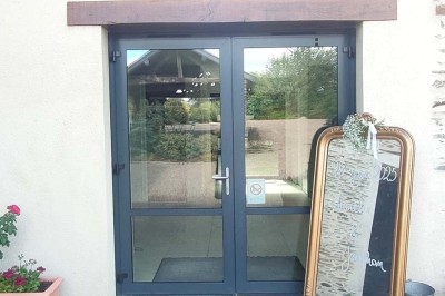 Voiture ancienne blanche décorée de fleurs, stationnée devant un bâtiment en pierre avec un toit en ardoise.