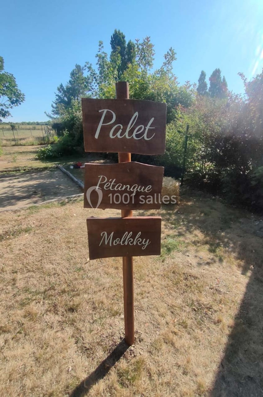 Panneau en bois indiquant ’Palet’, ’Pétanque’ et ’Mölkky’, installé sur une pelouse en extérieur.