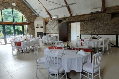 Voiture ancienne blanche décorée de fleurs, stationnée devant un bâtiment en pierre avec un toit en ardoise.