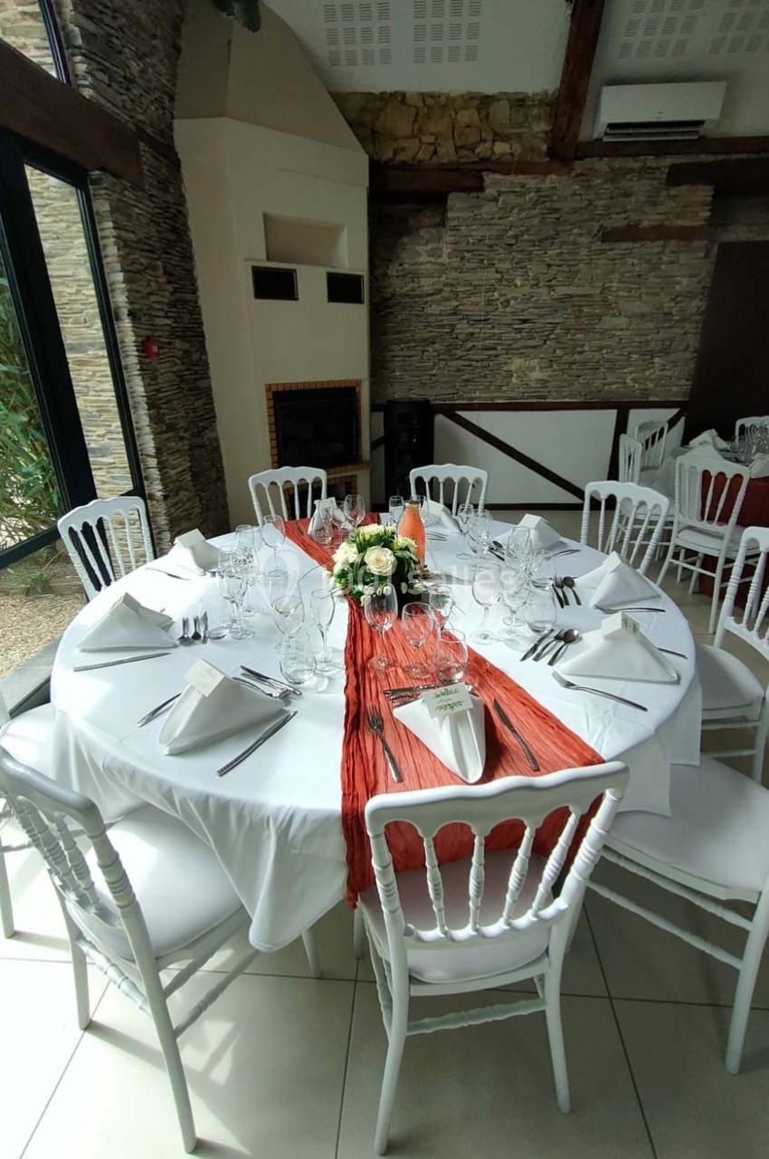 Table ronde dressée pour un repas, avec nappe blanche, chemin de table rouge, vaisselle élégante et centre floral.