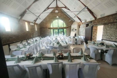 Voiture ancienne blanche décorée de fleurs, stationnée devant un bâtiment en pierre avec un toit en ardoise.