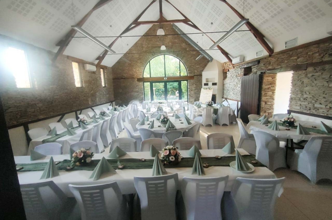 Salle de réception avec tables dressées, nappes blanches, serviettes vertes pliées et décorations florales.