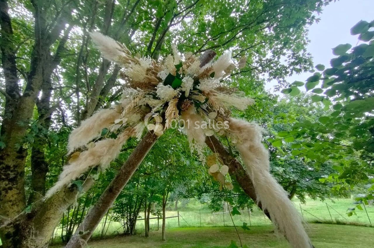 Structure décorative en bois ornée de fleurs séchées et de feuillages, installée dans un jardin verdoyant.