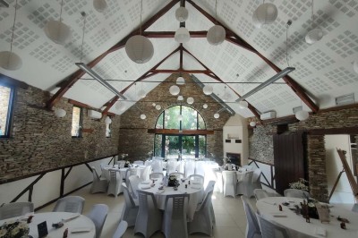 Voiture ancienne blanche décorée de fleurs, stationnée devant un bâtiment en pierre avec un toit en ardoise.