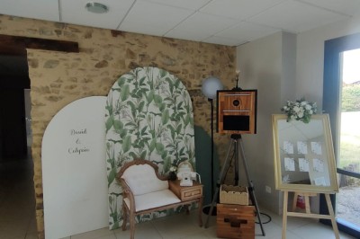Voiture ancienne blanche décorée de fleurs, stationnée devant un bâtiment en pierre avec un toit en ardoise.