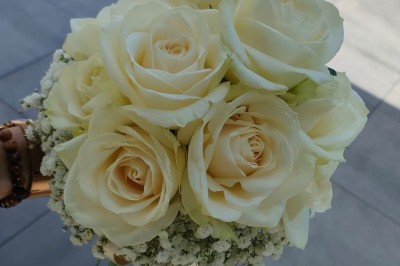 Voiture ancienne blanche décorée de fleurs, stationnée devant un bâtiment en pierre avec un toit en ardoise.