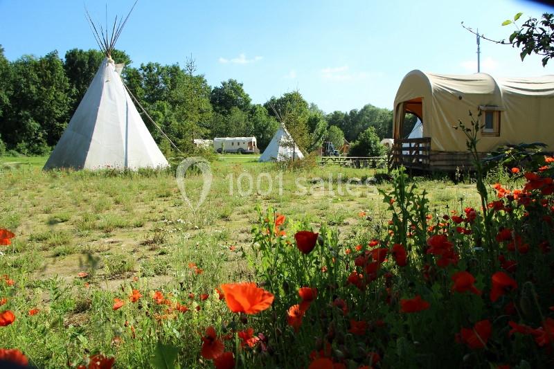 Prairie avec des tipis, une roulotte et des coquelicots, entourée d'arbres sous un ciel dégagé.