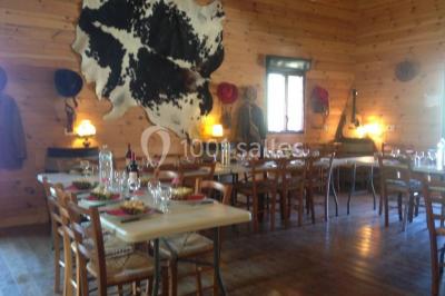 Bâtiments en bois avec une chapelle, une roulotte et des bottes de foin, entourés de verdure.