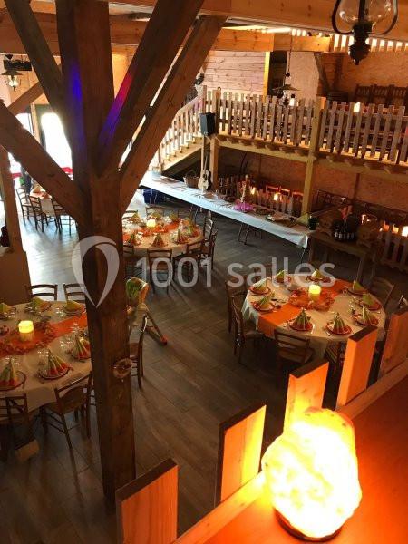 Salle de réception en bois avec tables rondes décorées, éclairage chaleureux et mezzanine visible en arrière-plan.