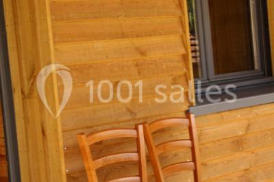 Bâtiments en bois avec une chapelle, une roulotte et des bottes de foin, entourés de verdure.