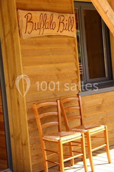 Deux chaises en bois devant une façade en bois avec une enseigne ’Buffalo Bill’ au-dessus d'une fenêtre.