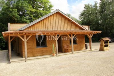 Bâtiments en bois avec une chapelle, une roulotte et des bottes de foin, entourés de verdure.