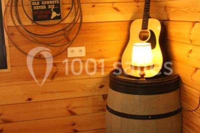 Bâtiments en bois avec une chapelle, une roulotte et des bottes de foin, entourés de verdure.